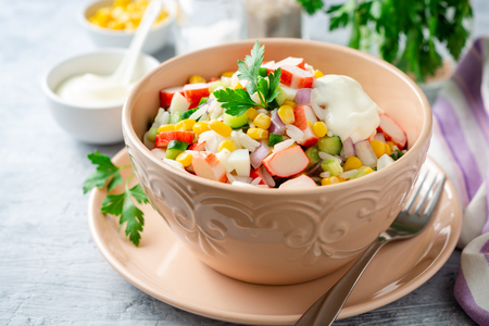 Salad with crab sticks, sweet corn, cucumbers, boiled eggs, onion and rice in bowl on concreteの写真素材