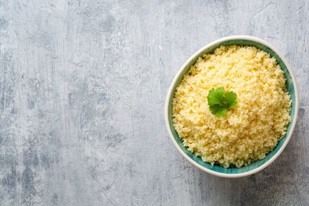 Cooked couscous with cilantro in ceramic bowl on concrete