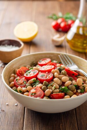 White bean salad with tomatoes, capers, garlic and parsley in bowl on wooden table. Selective focus.の写真素材