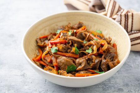 Fried chicken gizzards with carrot and onion in bowl on concrete
