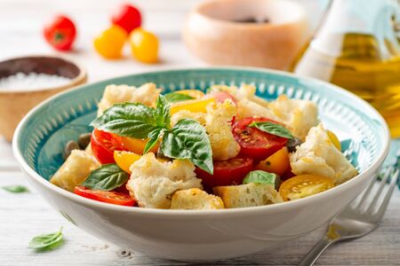 Traditional Italian salad Panzanella with cherry tomatoes, bread, capers and basil in bowl on wooden table. Selective focus.の写真素材