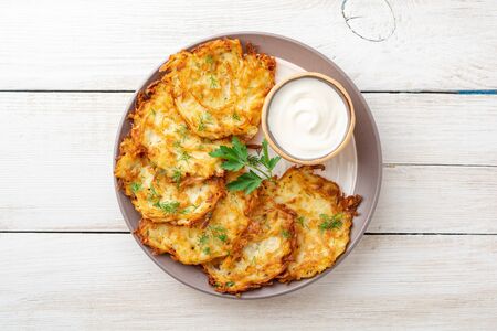 Potato pancakes or latkes or draniki with sour cream in plate on white wooden table. Top view. Copy...