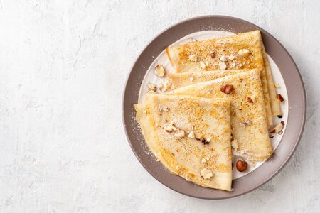 Crepes with hazelnuts and powdered sugar on plate on white concrete background. Top view. Copy space.の写真素材