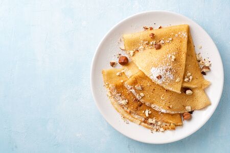 Crepes with hazelnuts and powdered sugar on white plate on blue concrete background. Top view. Copy space.の写真素材