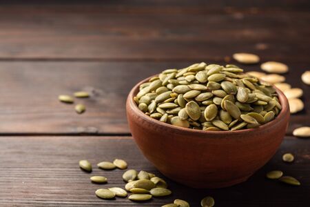 Pumpkin seeds in ceramic bowl on dark woodenの写真素材