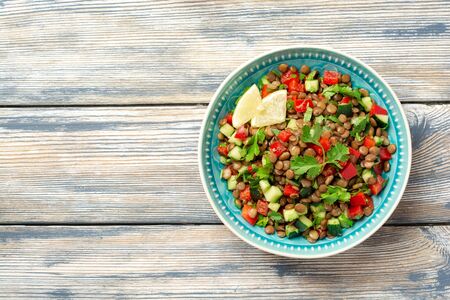 Lentil salad with cucumber, bell pepper and coriander leaves on rustic wooden table. Top view, copy space.の写真素材