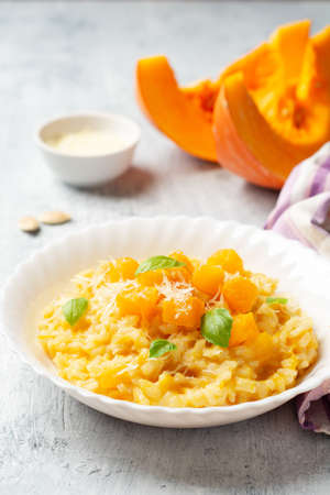 Pumpkin risotto with parmesan cheese and basil leaves on concrete background. Selective focus.の写真素材
