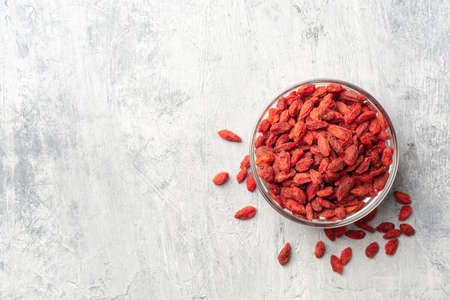 Dry goji berries in glass bowl on concrete background. Top view, copy space.