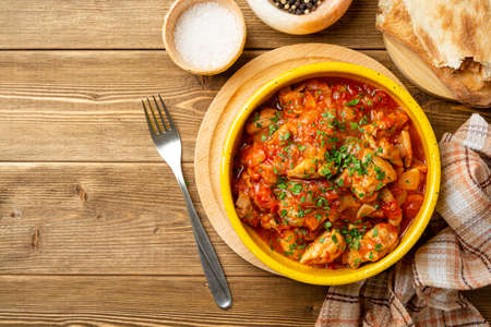 Traditional georgian dish Chakhokhbili. Chicken stew with tomatoes in ceramic bowl on wooden background. Top view, copy space.の写真素材