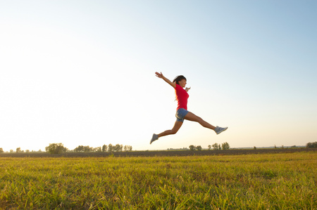 Young woman with raised arms outdoor jumpingの写真素材