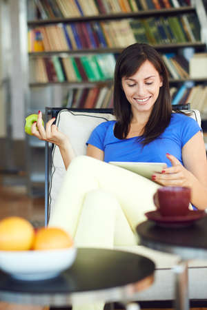 Young woman eating apple and surfing internet over digital laptop in apartment