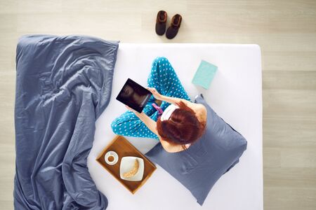 Young woman surfing on the digital tablet in bed, aerial viewの写真素材