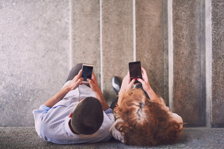 Couple using smart phones leaned on the wall, focus on their headsの写真素材