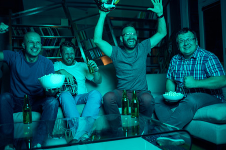 Four men watching american football game on televisionの写真素材