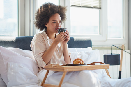 Young woman sitting on bed, drinking coffeeの写真素材