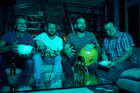 Four friends watching game of american football on televisionの写真素材