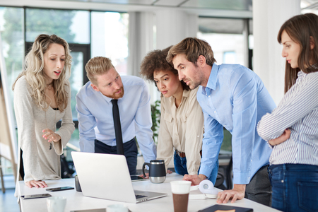 Small group of business people standing in office, looking at laptop and developing business plan. Start up business concept.の写真素材