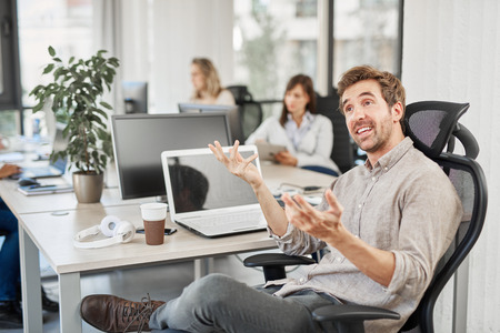 Portrait of CEO talking to employee while sitting in office. In background coworkers doing their...