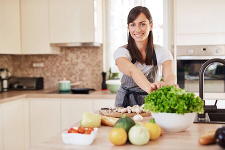 Beautiful hardworking housewife taking salad from bowl while standing in kitchen. Home made dinner preparation concept.の写真素材