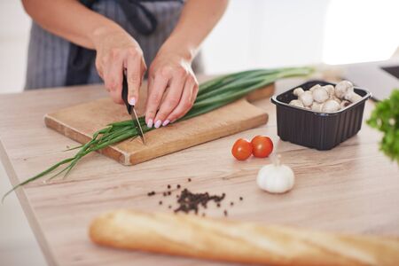 Cut out picture of woman chopping leek on cutting board in kitchen.の写真素材