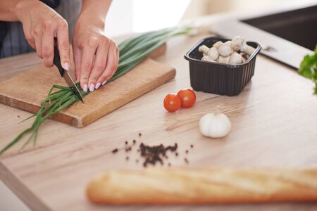 Cut out picture of woman chopping leek on cutting board in kitchen.の写真素材