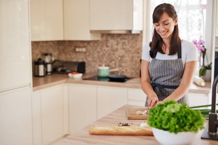 Smiling Caucasian female chef in apron chopping leek in kitchen and preparing dinner. Preparation of domestic food concept.の写真素材