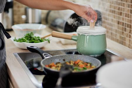 Dedicated Caucasian woman opening boiling pot. Vegetarian dinner preparation concept.の写真素材