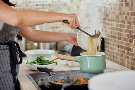 Caucasian woman in apron standing next to stove and preparing spaghetti. Preparation of italian food concept.の写真素材