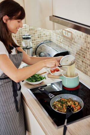 Caucasian woman in apron standing next to stove and preparing spaghetti. Preparation of italian food concept.の写真素材