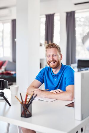 Cheerful Caucasain ginger employee sitting in his office and writing his tasks in notebook.の写真素材