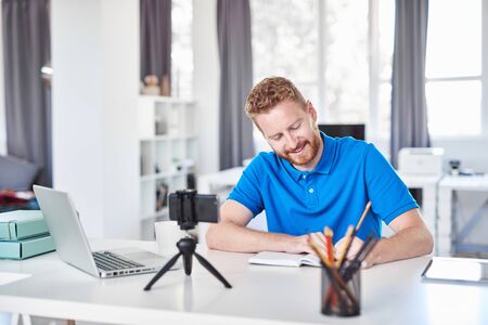 Cheerful Caucasain ginger employee sitting in his office and writing his tasks in notebook.の写真素材