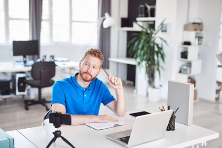Handsome Caucasian ginger employee dressed casual sitting in office and thinking about solution for problem. Start up business concept.の写真素材