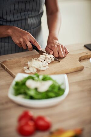 Close up of mixed race woman in apron standing in kitchen and chopping mushrooms.の写真素材