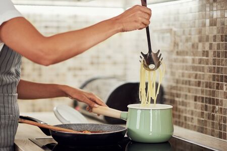 Cropped picture of mixed race woman in apron standing next to stove and making spaghetti.の写真素材