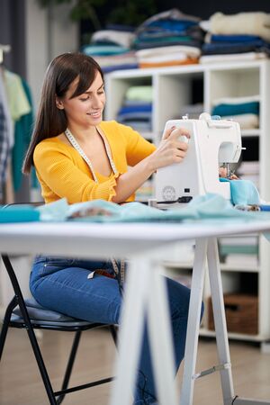 Smiling charming caucasian fashion designer sitting in her studio and sewing beautiful evening dress.の写真素材