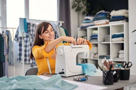Dedicated seamstress sitting in her studio and inserting thread in sewing machine.の写真素材