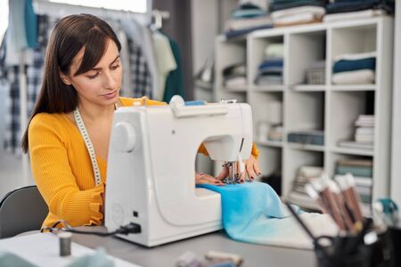 Focused charming caucasian fashion designer sitting in her studio and sewing beautiful evening dress.の写真素材