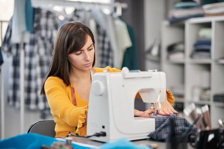 Focused charming caucasian fashion designer sitting in her studio and sewing beautiful evening dress.の写真素材