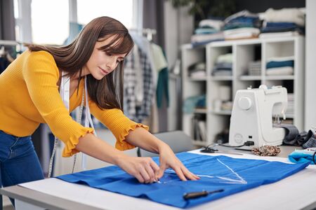 Creative caucasian fashion designer standing in her studio and drawing scheme on blue linen for a beautiful night dress.の写真素材