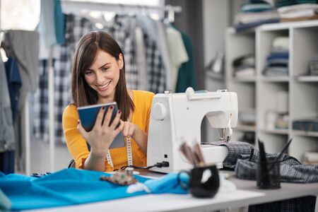 Smiling positive caucasian brunette sitting in her fashion studio and using tablet.の写真素材