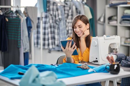 Smiling positive caucasian brunette sitting in her fashion studio and using tablet.の写真素材