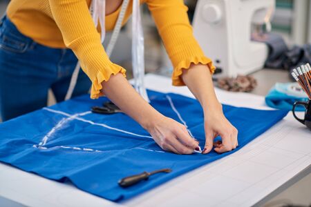 Creative caucasian fashion designer standing in her studio and drawing scheme on blue linen for a beautiful night dress.の写真素材
