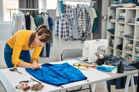 Focused beautiful caucasian seamstress putting pin on seam and making beautiful skirt.の写真素材