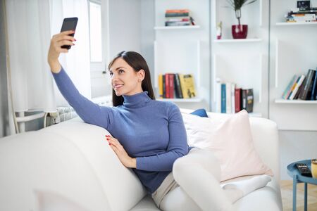 Young attractive smiling brunette taking selfie. She is gonna post on social media.の写真素材