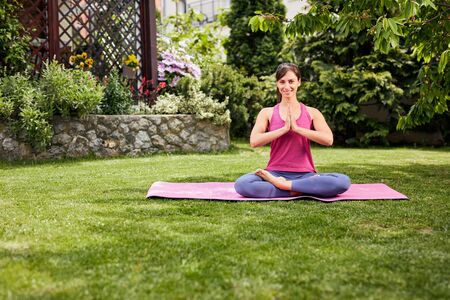 Young attractive brunette sitting in her backyard in lotus position and meditating.の写真素材