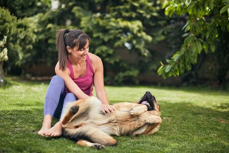Young attractive fit yogi brunette playing with her dog in backyard.の写真素材