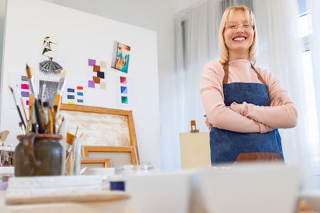 Portrait of smiling female artist standing with arms crossed in creative studioの写真素材