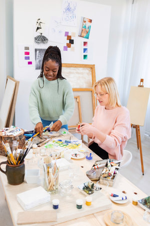 Portrait of multiethnic female artist and her colleague painting in studioの写真素材