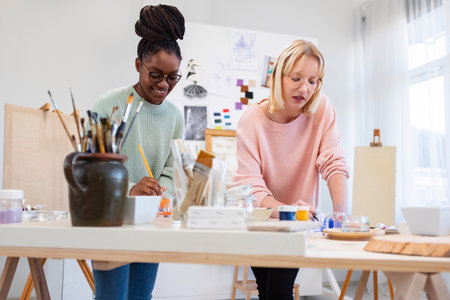 Portrait of young female artist working with her colleague in creative studioの写真素材