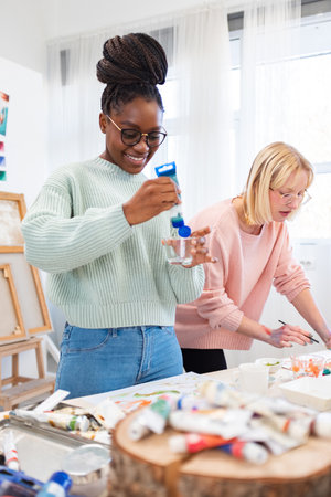 Creative female artist painting a picture in her studio with her colleagueの写真素材